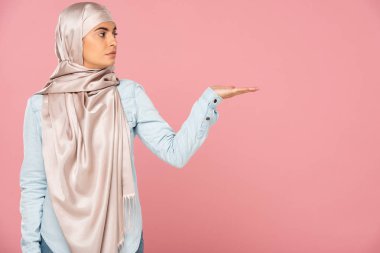 türban güzel müslüman kadın bir şey sunan, pembe izole 