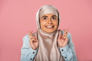 parmakları çapraz ile hijab neşeli müslüman kadın, pembe izole 
