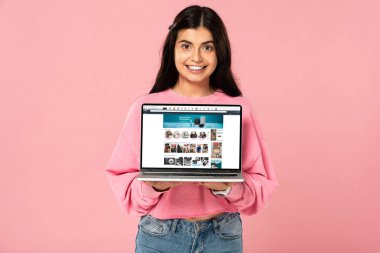 Kiev, Ukrayna - 30 Temmuz 2019: ekranda amazon web sitesi ile dizüstü bilgisayar tutan gülümseyen kız, pembe izole