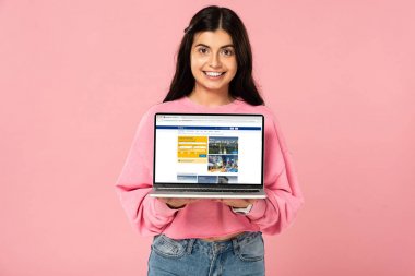 Kiev, Ukrayna - 30 Temmuz 2019: ekranda rezervasyon web sitesi ile dizüstü bilgisayar tutan gülümseyen kız, pembe izole