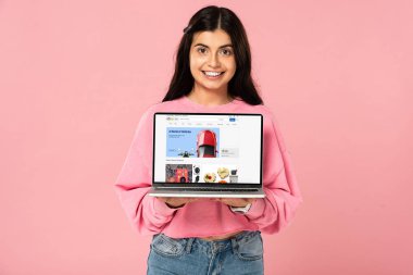 Kiev, Ukrayna - 30 Temmuz 2019: ekranda ebay web sitesi ile dizüstü bilgisayar tutan gülümseyen kız, pembe izole