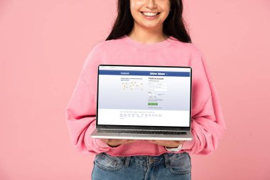 Kiev, Ukrayna - 30 Temmuz 2019: ekranda facebook web sitesi ile dizüstü bilgisayar tutan gülümseyen kız kırpılmış görünümü, pembe izole