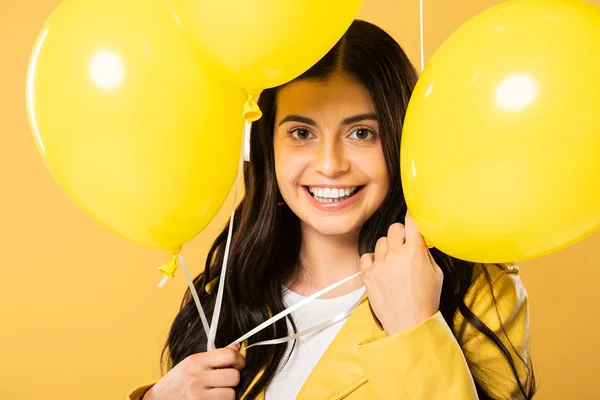 smiling woman holding yellow balloons, isolated on yellow