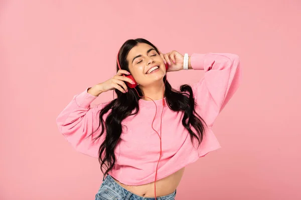 ピンクに隔離されたヘッドフォンで音楽を聴く幸せな女性 — ストック写真