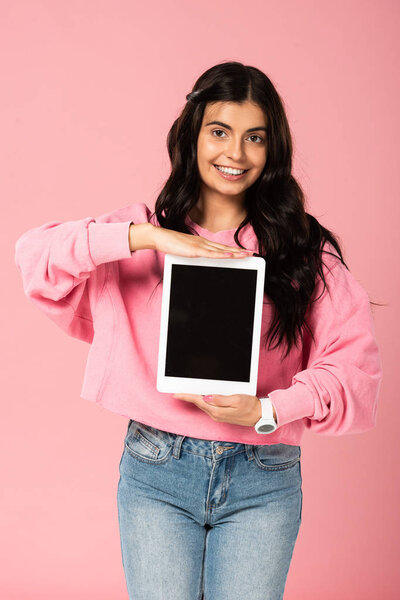 smiling girl presenting digital tablet with blank screen, isolated on pink