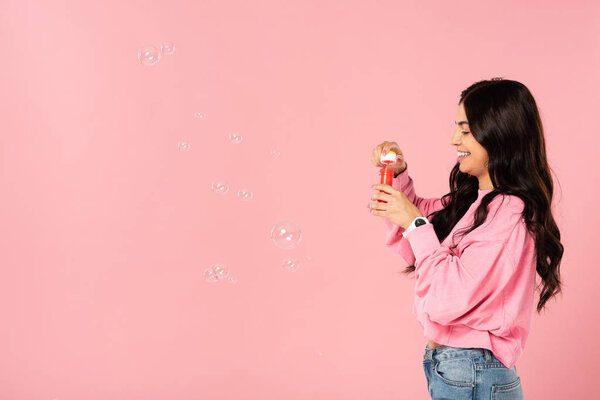 cheerful girl blowing soap bubbles isolated on pink