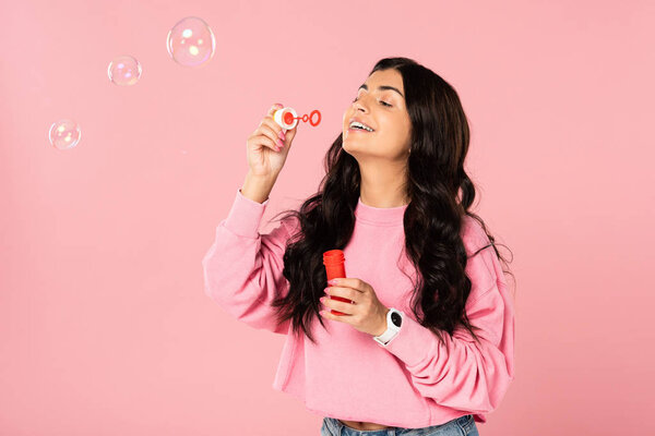 beautiful brunette girl blowing soap bubbles isolated on pink