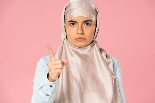 serious muslim woman in hijab pointing at you, isolated on pink 