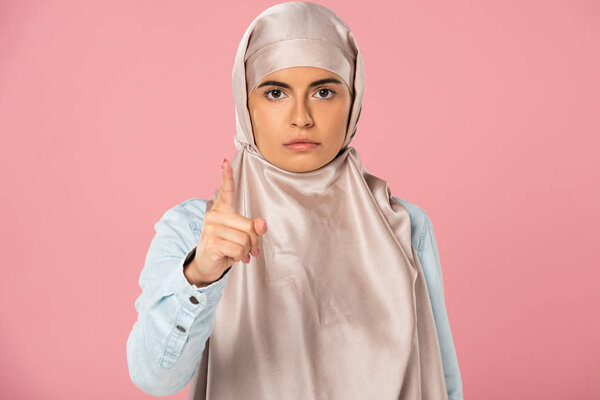 serious arabic woman in hijab pointing at you, isolated on pink 