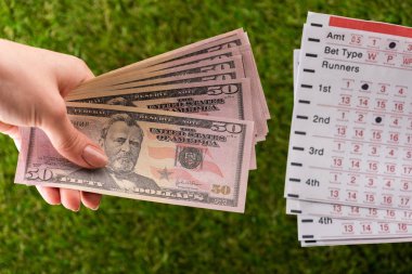 Yeşil çimenler ve spor bahisleri üzerine bahis listelerinin yanında dolar banknotları tutan bir kadın.