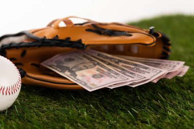Beyazlara izole edilmiş yeşil çimenler üzerine beysbol eldivenindeki dolar banknotlarının seçici odağı, spor bahisleri konsepti