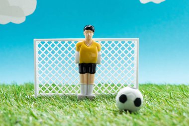 Minyatür futbol kapılarının yanındaki oyuncak kaleci ve mavi arka planda bulutlu top, spor bahisleri konsepti
