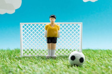 toy goalkeeper near miniature football gates and ball on blue background with clouds, sports betting concept clipart