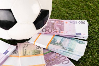 Yeşil çimlerin üzerinde futbol topu, spor bahisleri ve dolar banknotlarının seçici odak noktası