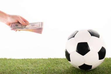 Amerikan futbolu topunun yanında dolar banknotları olan, beyazlar üzerinde izole edilmiş, spor bahisleri konsepti olan bir kadın eli.