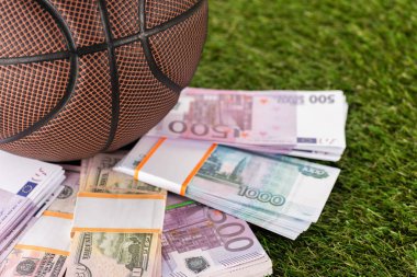 close up view of basketball ball near dollar and euro banknotes on green grass, sports betting concept clipart