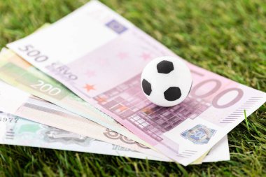 Oyuncak futbol topunun ve yeşil çimlere Avro banknotlarının seçici odak noktası, spor bahisleri konsepti