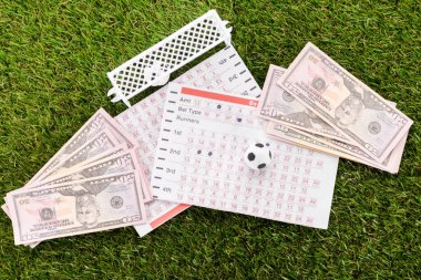 Oyuncak futbol kapılarının ve neredeyse dolar değerinde banknotların ve yeşil çimenlerin bahis listelerinin en üst görüntüsü, spor bahisleri konsepti