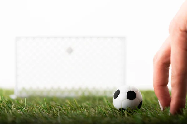 白いスポーツの賭けの概念に隔離された緑のフィールド上のおもちゃのサッカーの門とボールの近くの女性の指のクロップドビュー — ストック写真