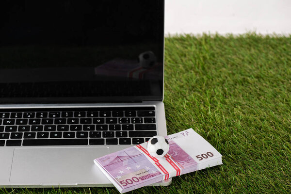 toy soccer ball and euro banknotes on laptop with blank screen on green grass isolated on white, sports betting concept
