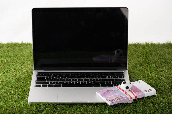 toy soccer ball and euro banknotes on laptop with blank screen on green grass isolated on white, sports betting concept