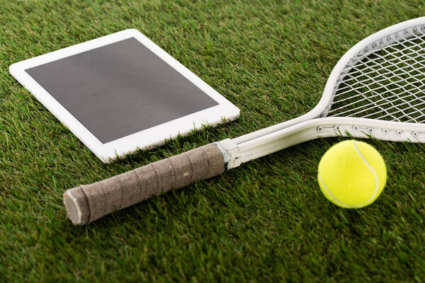 tennis racket and ball near digital tablet with blank screen on green grass, sports betting concept