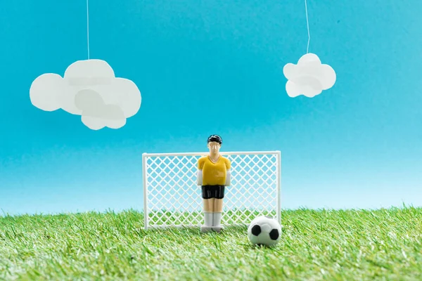 Mavi arkaplanlı minyatür futbol kalecisi, bulutlu futbol sahası, spor bahisleri konsepti