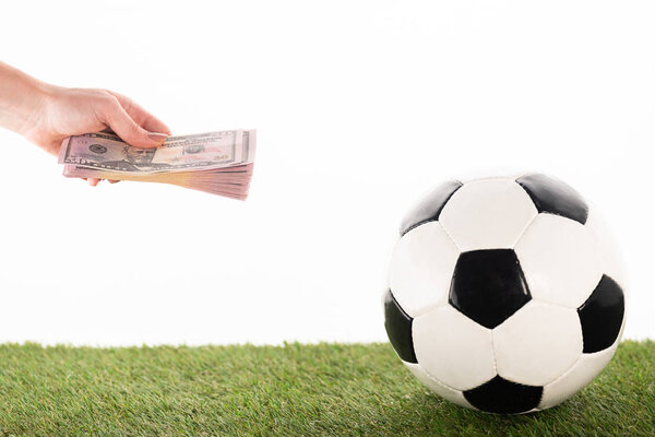 cropped view of female hand with dollar banknotes near soccer ball on green grass isolated on white, sports betting concept