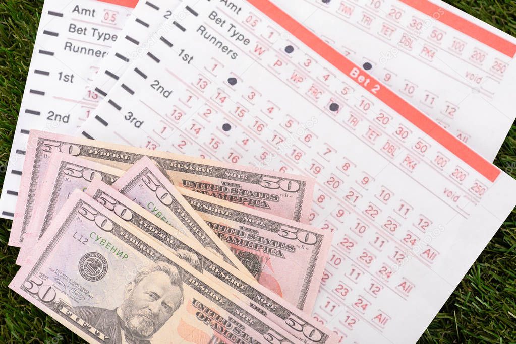Dollar banknotes and betting lists on green grass, sports betting concept