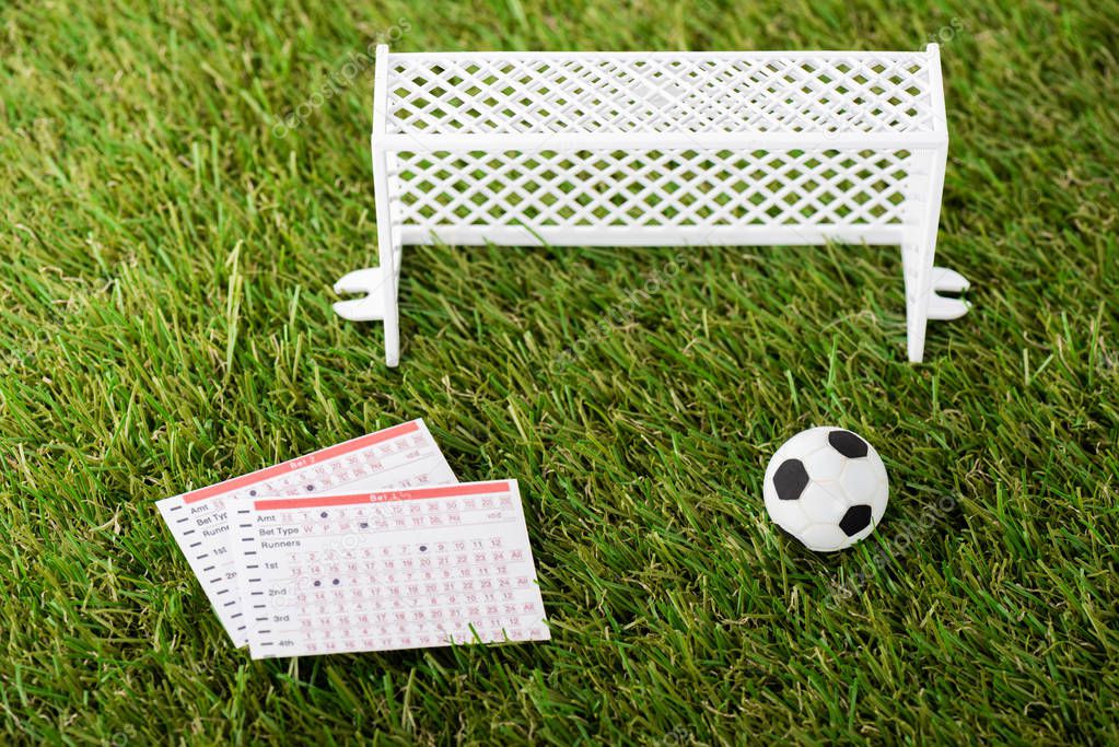 toy soccer ball near miniature football gates and betting lists on green grass, sports betting concept
