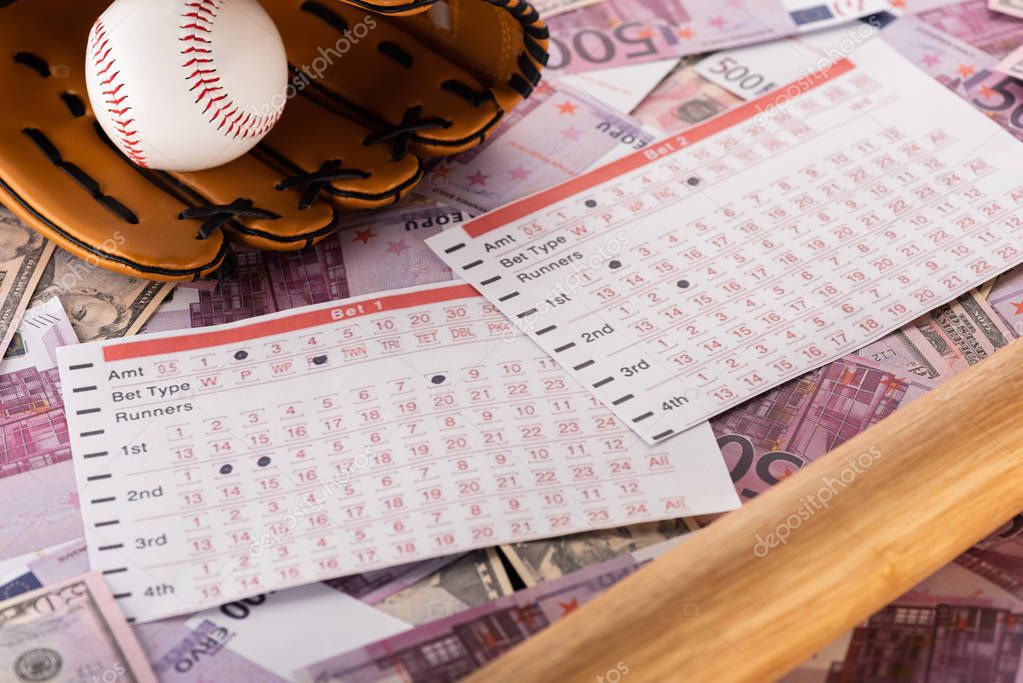 Betting lists near baseball bat, glove and ball on euro and dollar banknotes, sports betting concept
