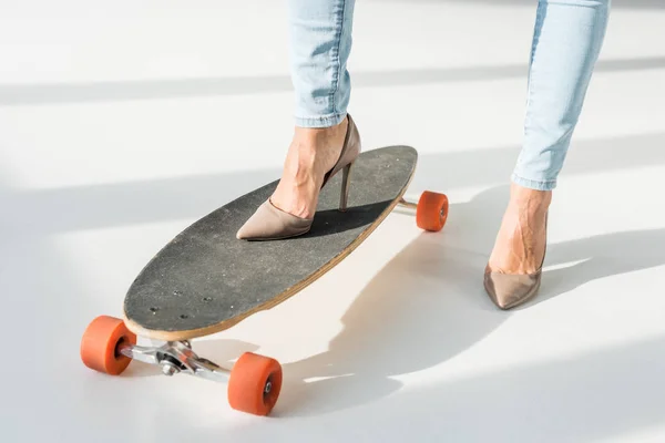 Обрізаний вид жінки на високих підборах, що кладе ногу на скейтборд на сірому фоні — стокове фото