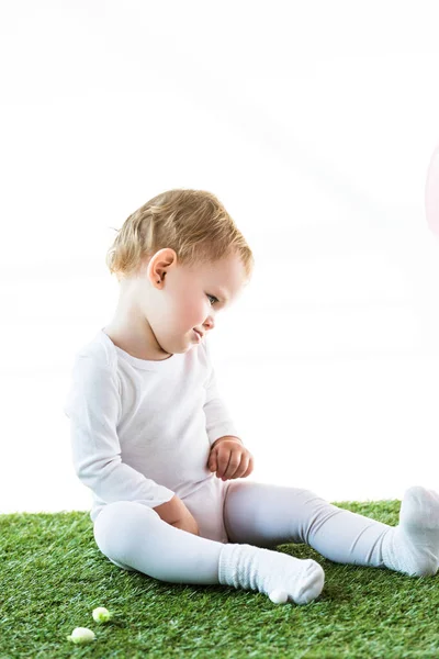 Entzückendes blondes Kind sitzt auf grünem Gras isoliert auf weißem Grund — Stockfoto