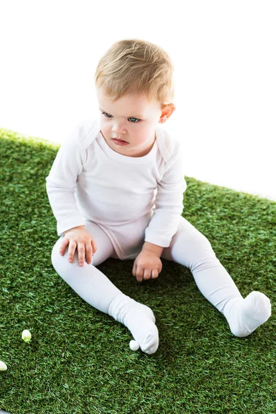 Mignon enfant avec des cheveux blonds assis sur l'herbe verte isolé sur blanc — Photo de stock