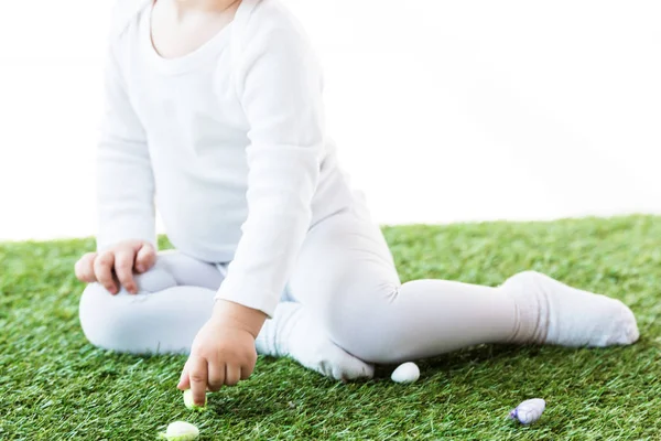 Vista parziale del bambino seduto sull'erba verde vicino alle uova di quaglia colorate isolate sul bianco — Foto stock