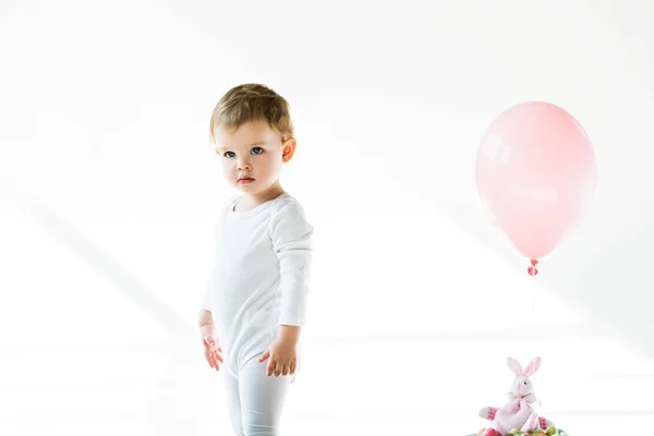 Adorable kid standing near toy bunny with pink air balloon isolated on white — Stock Photo