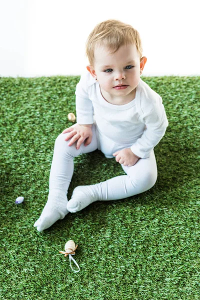 Mignon blond enfant assis sur herbe verte et regardant loin isolé sur blanc — Photo de stock