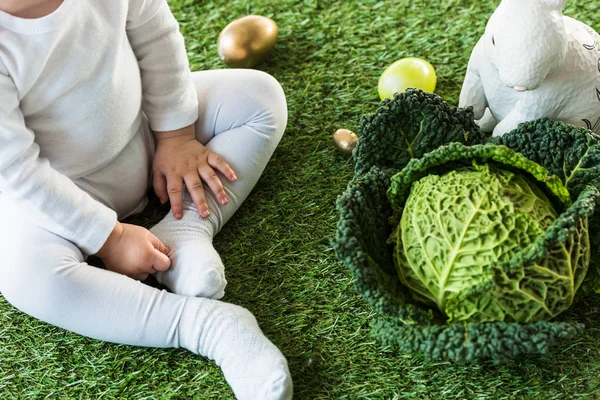 Teilansicht eines Kindes, das in der Nähe von Ostereiern, Wirsing und Zierhasen sitzt — Stockfoto