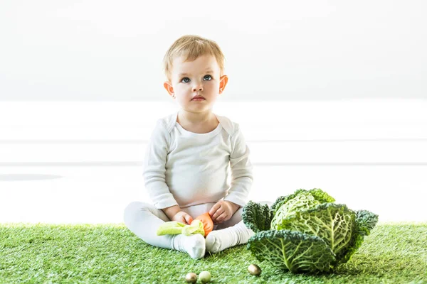 Adorabile bambino seduto sull'erba verde vicino alle uova di quaglia d'oro e verza — Foto stock