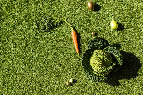 Vue du dessus des œufs de Pâques colorés, du chou de Savoie et de la carotte sur herbe verte — Photo de stock