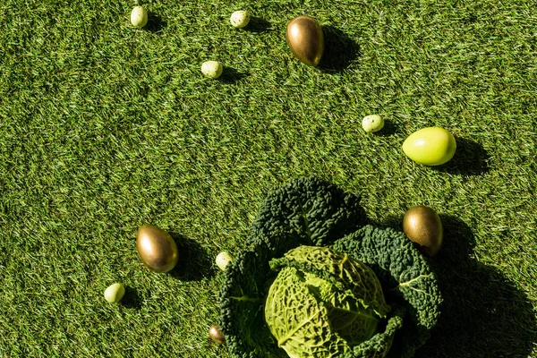 Верхний вид разноцветных куриных и перепелиных яиц и савойской капусты на зеленой траве — стоковое фото