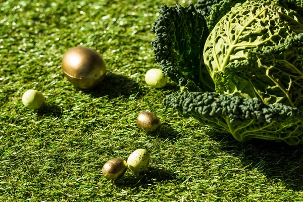 Golden Easter eggs and savoy cabbage on green grass — Stock Photo