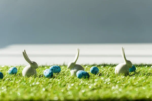 Enfoque selectivo de conejos decorativos y huevos de codorniz azul en la superficie de la alfombra de hierba verde - foto de stock