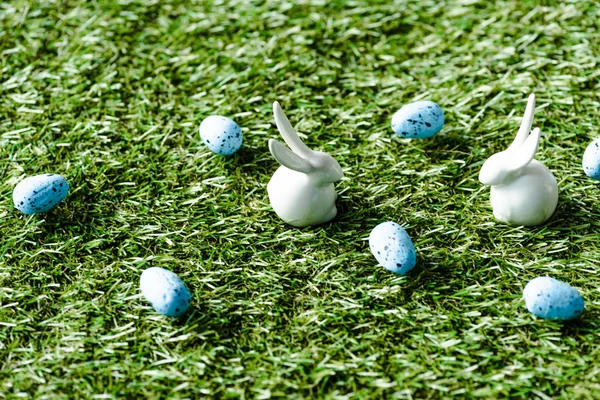 Decorative rabbits and blue quail eggs on green grass surface — Stock Photo