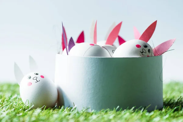 Caja con huevos de Ester con caras divertidas de conejo y orejas de papel en blanco - foto de stock