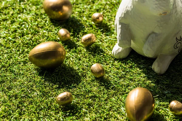 Golden Easter eggs and decorative rabbit on green grass surface — Stock Photo