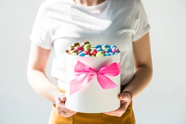 Vista recortada de la mujer sosteniendo caja redonda llena de coloridos huevos de Pascua aislados en gris - foto de stock