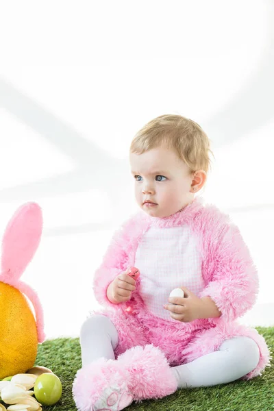 Милый ребенок в розовом пушистом костюме с разноцветными перепелиными яйцами, изолированными на белом — стоковое фото