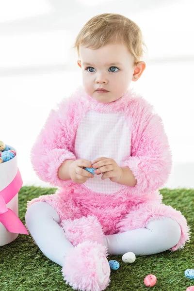 Cute dreamy kid in pink fluffy costume sitting near box with Easter eggs isolated on white — Stock Photo