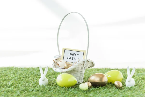Uova di Pasqua colorate, conigli decorativi e cesto di paglia con felice biglietto di Pasqua isolato su bianco — Foto stock